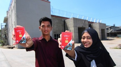 Mahasiswa memegang smart card di depan bangunan kampus